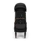 Nuna TRVL 360 lightweight travel stroller in Caviar black, shown in a front view against a clean white background. The stroller features an extended sun canopy, a brown leatherette-accented pushbar and rotating armbar, a harness with a magnetic buckle, 360-degree swivel wheels, and an under-seat storage basket.