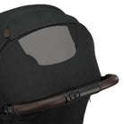 Nuna TRVL 360 lightweight travel stroller in Caviar black, shown in a folded, freestanding position against a clean white background with a brown leatherette pushbar visible at the top.