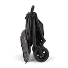 Nuna TRVL 360 lightweight travel stroller in Pewter grey, shown in a folded, freestanding position against a clean white background with a brown leatherette pushbar visible at the top.