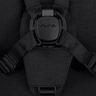 Close-up of a black car seat with Nuna logo on the buckle area against a dark background.