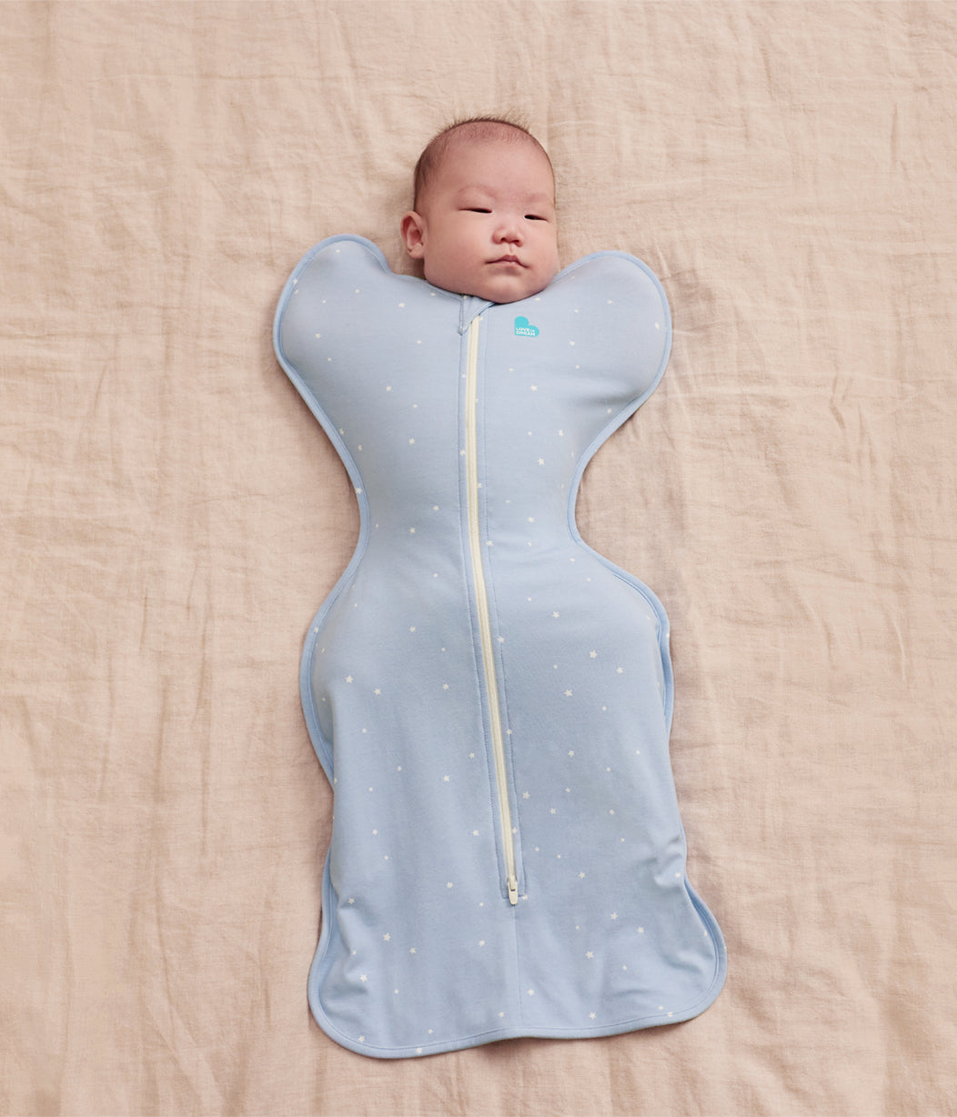 Baby wrapped in a light blue swaddle with star patterns on a beige surface