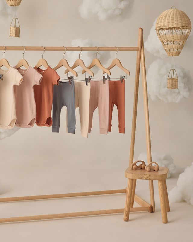 Children's leggings in various colors hanging on a wooden rack with a small wooden stool below.