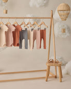 Children's leggings in various colors hanging on a wooden rack with a small wooden stool below.