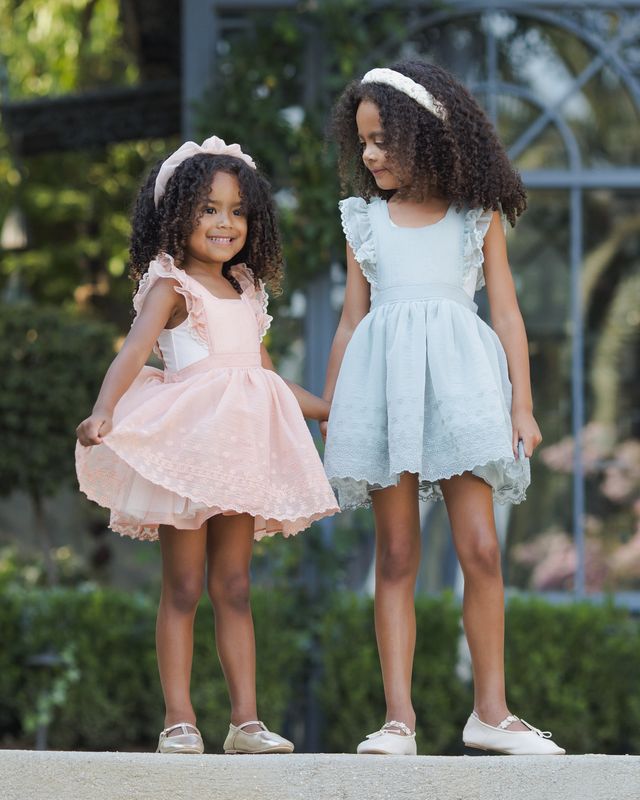 Two young girls in dresses standing outdoors with a blurred background