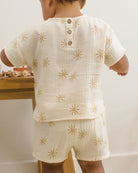 Child wearing a cream-colored outfit with gold star patterns indoors.