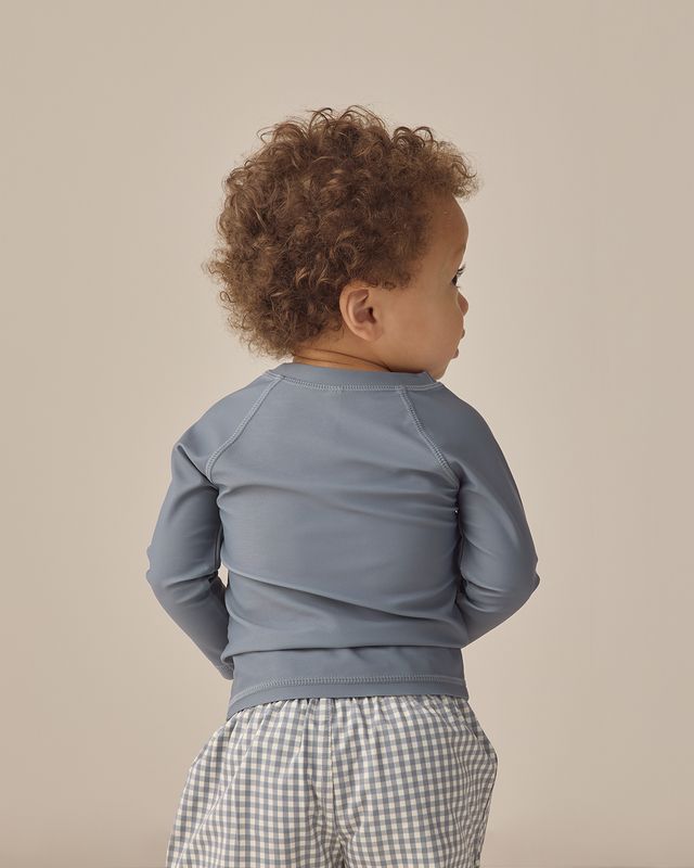 Child wearing a blue long-sleeve shirt and checkered pants on a beige background