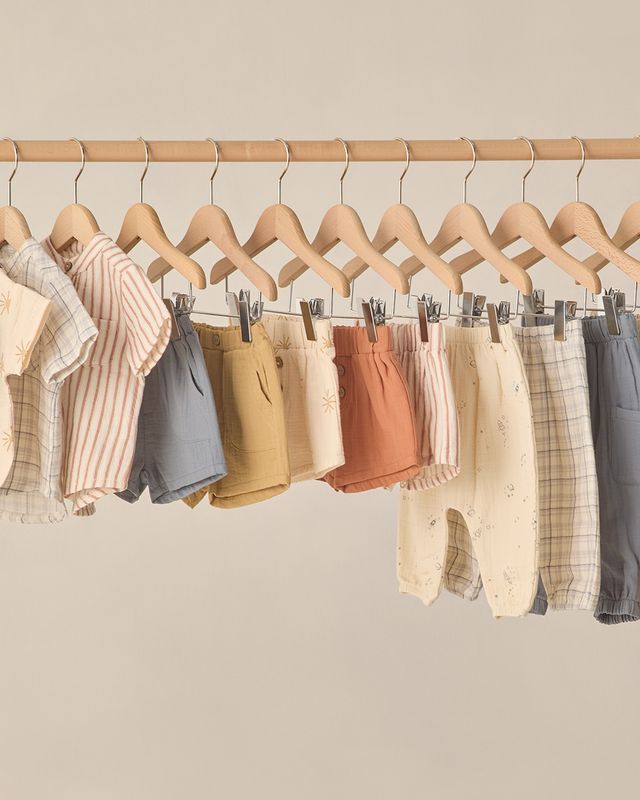 Row of children's clothing on wooden hangers against a beige wall