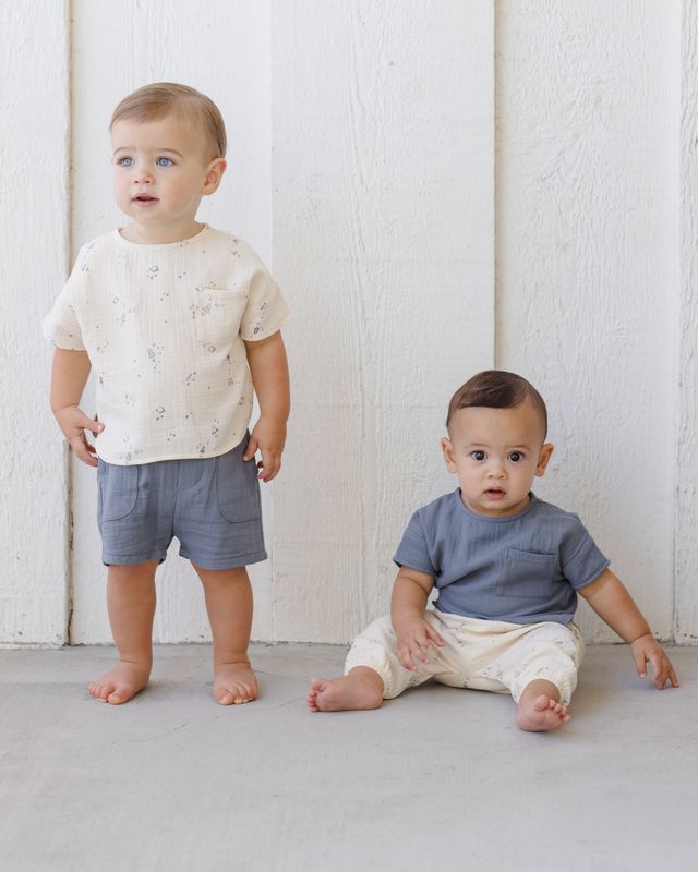 Two young children wearing matching outfits against a white wooden panel background