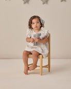Child sitting on a chair holding toy microphone against a neutral background