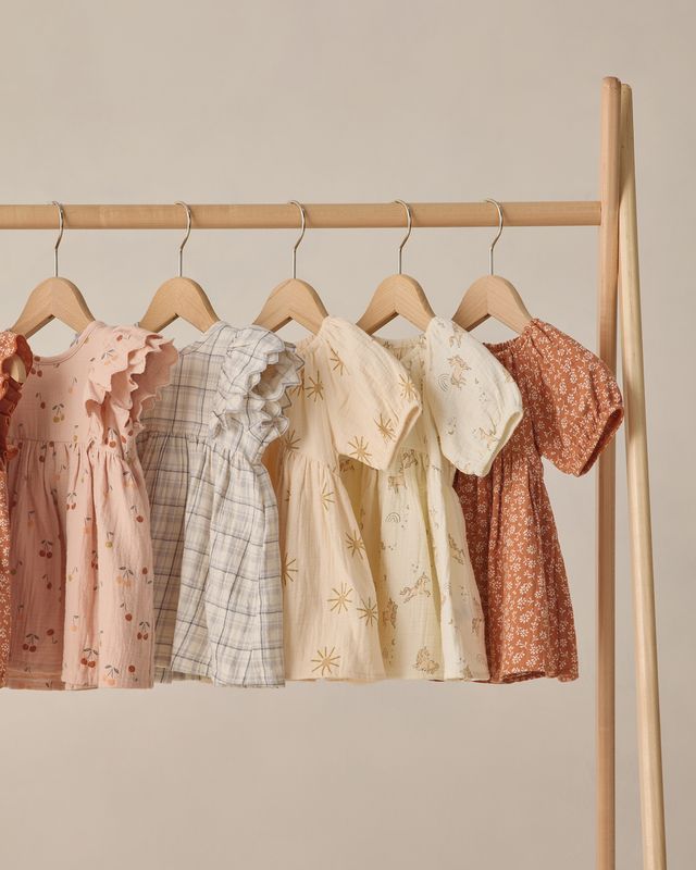 Five children's dresses hanging on a rack against a beige wall