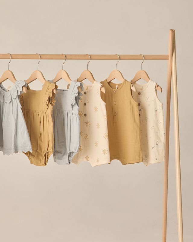 Set of baby rompers on hangers against a neutral background