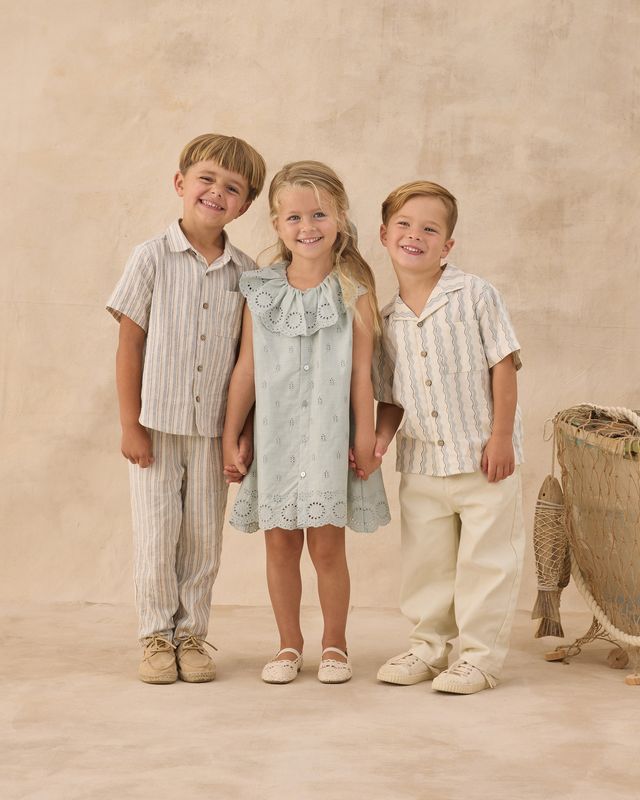Three children in matching outfits standing together against a beige background