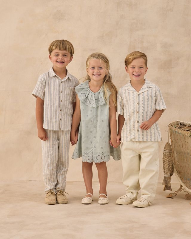 Three children in matching outfits standing together against a beige background