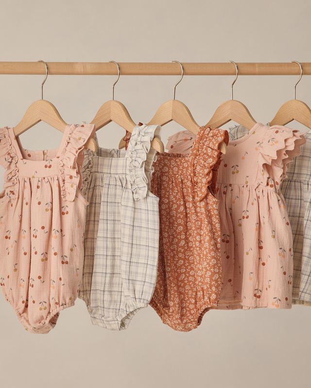 Collection of baby rompers on hangers against a neutral background