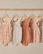Collection of baby rompers on hangers against a neutral background