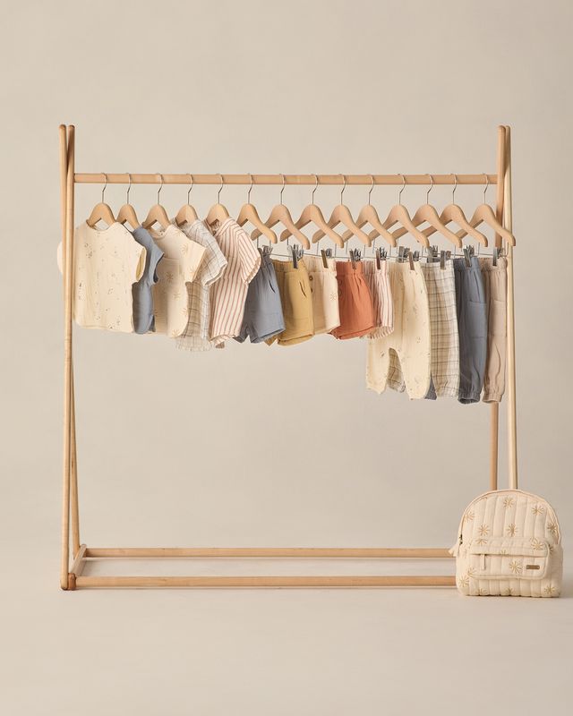 Wooden clothing rack with baby clothes on a beige background