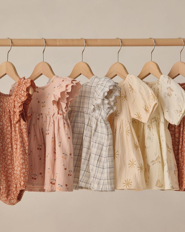 Row of baby dresses on hangers against a neutral background