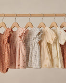 Row of baby dresses on hangers against a neutral background
