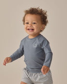 Child wearing a blue long-sleeve shirt with a logo on a beige background