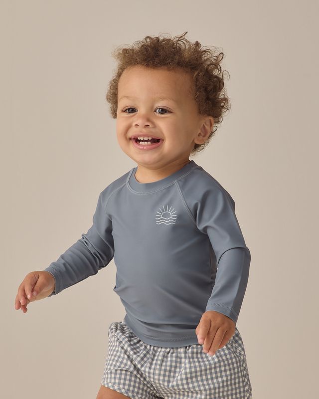 Child wearing a blue long-sleeve shirt with a logo on a beige background