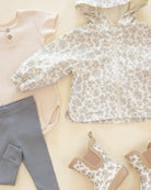 Children's clothing including a floral top, gray pants, and shoes on a light background