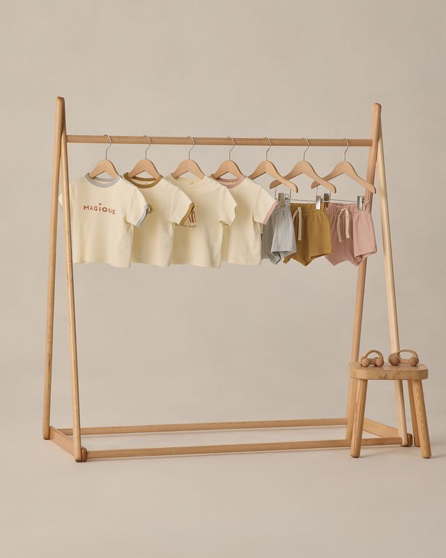 Wooden clothing rack with baby clothes on a beige background