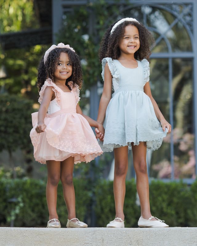 Two young girls in dresses standing outdoors with a blurred background