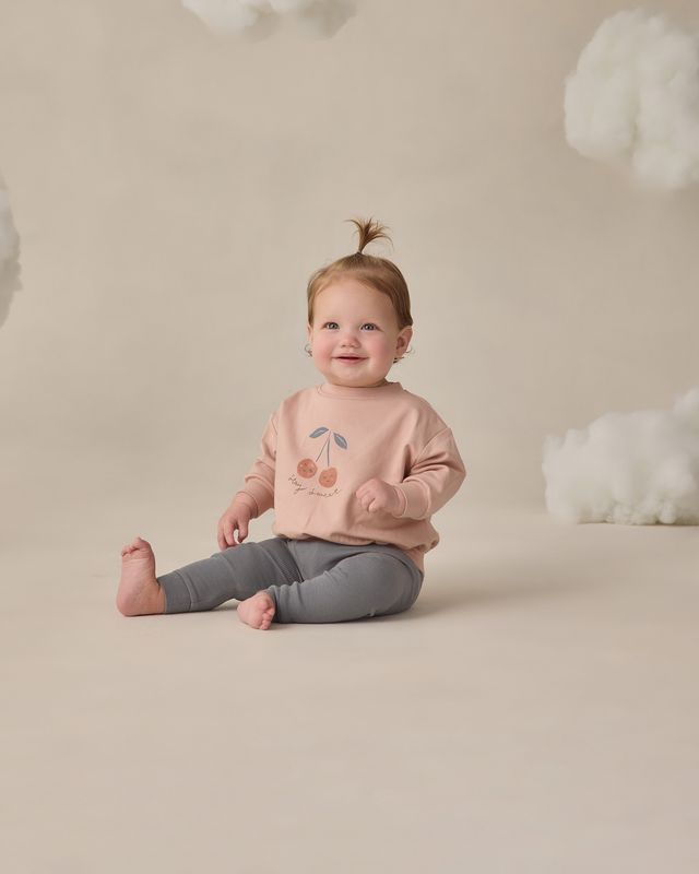 Child wearing a pink sweatshirt with a cherry design on a beige background