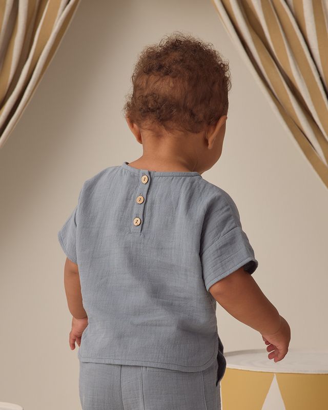 Child wearing a light blue shirt with buttons, standing against a neutral background