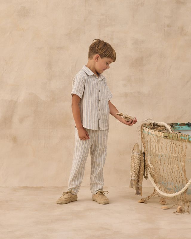 Young boy in striped shirt and pants standing next to a woven basket on a beige background
