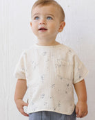 Baby wearing a light-colored shirt with subtle patterns against a white background
