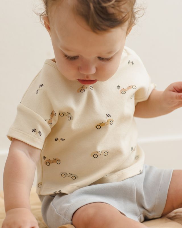 Child wearing a cream-colored shirt with car patterns on a neutral background