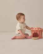 Baby playing with a small, decorative woven basket on a plain background