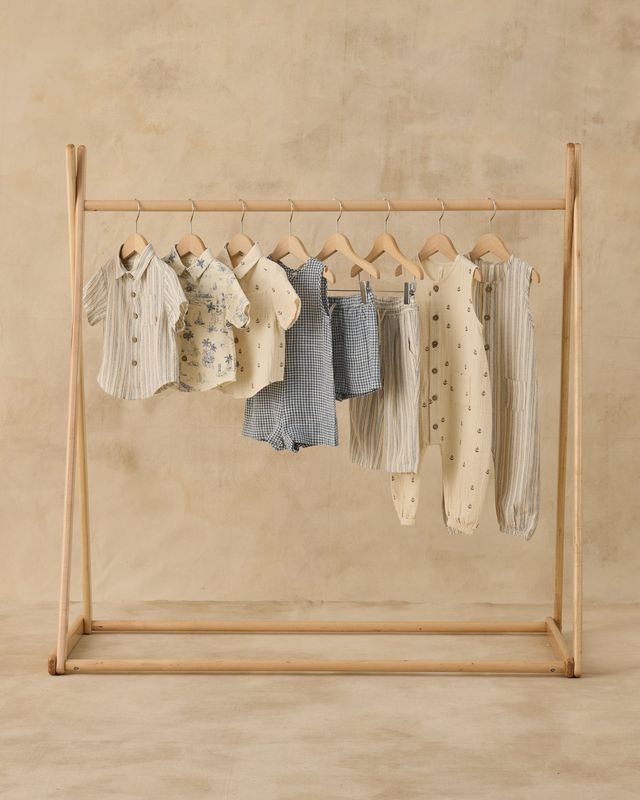 Wooden clothing rack with baby clothes on a beige background