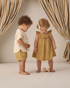 Two children, a boy and a girl, standing in front of striped curtains.