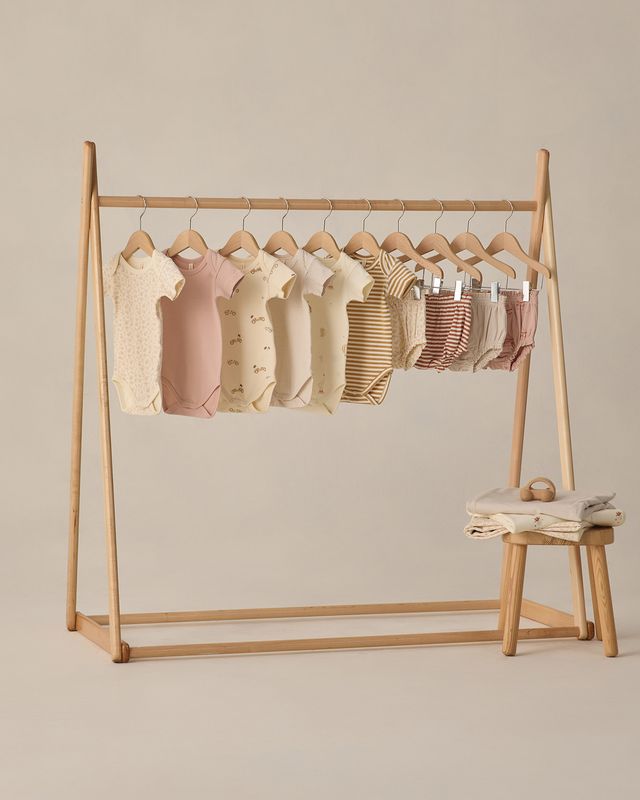 Wooden clothing rack with baby outfits on hangers against a beige background