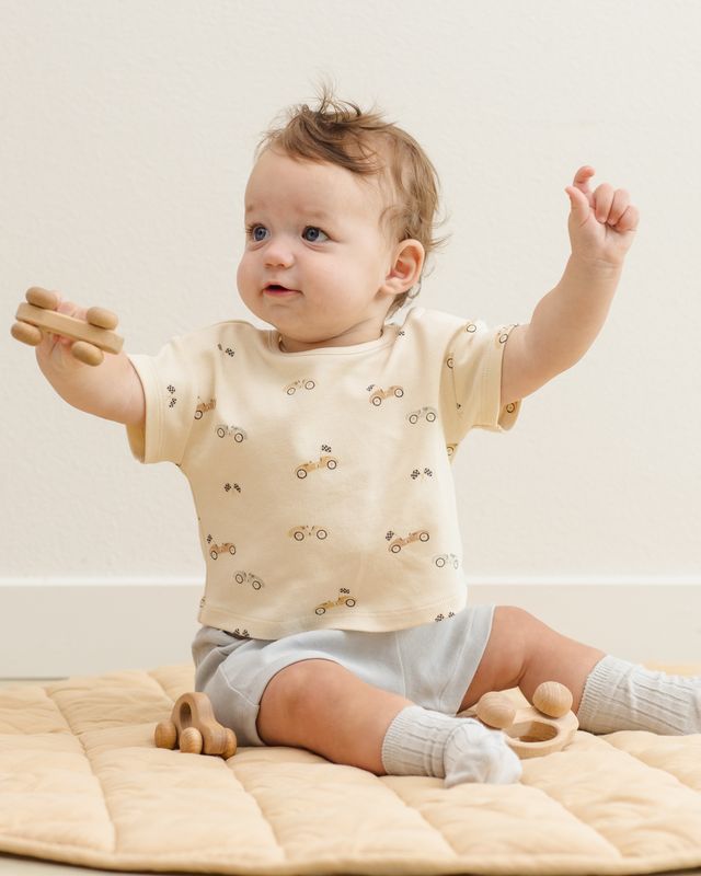 Baby wearing a cream-colored shirt with small patterns, sitting on a beige blanket.