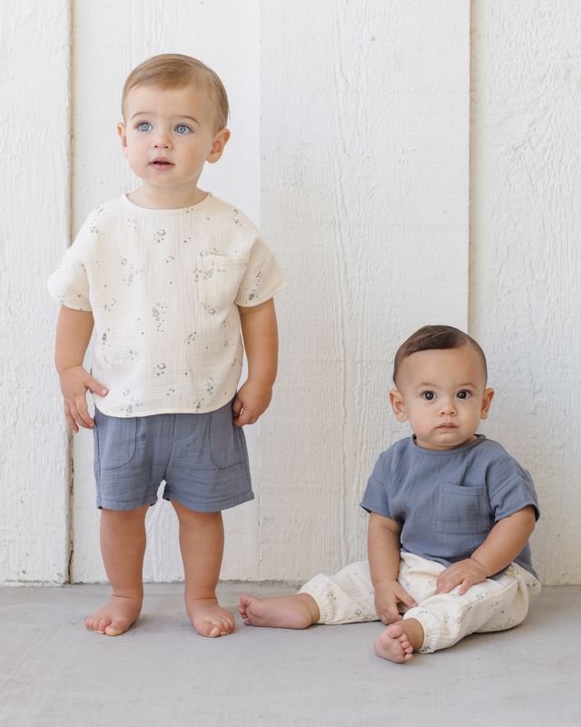 Two young children wearing matching outfits against a white wooden background