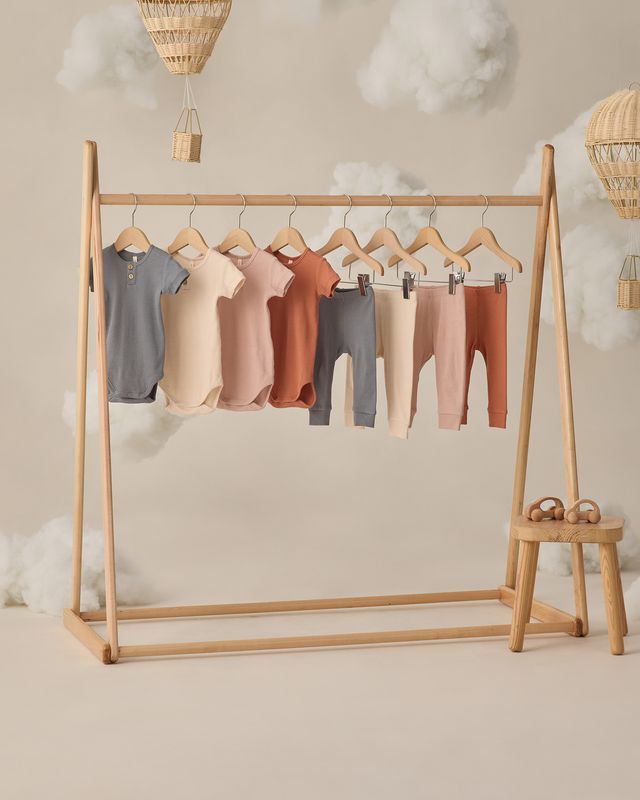 Wooden clothing rack with baby clothes on a neutral background