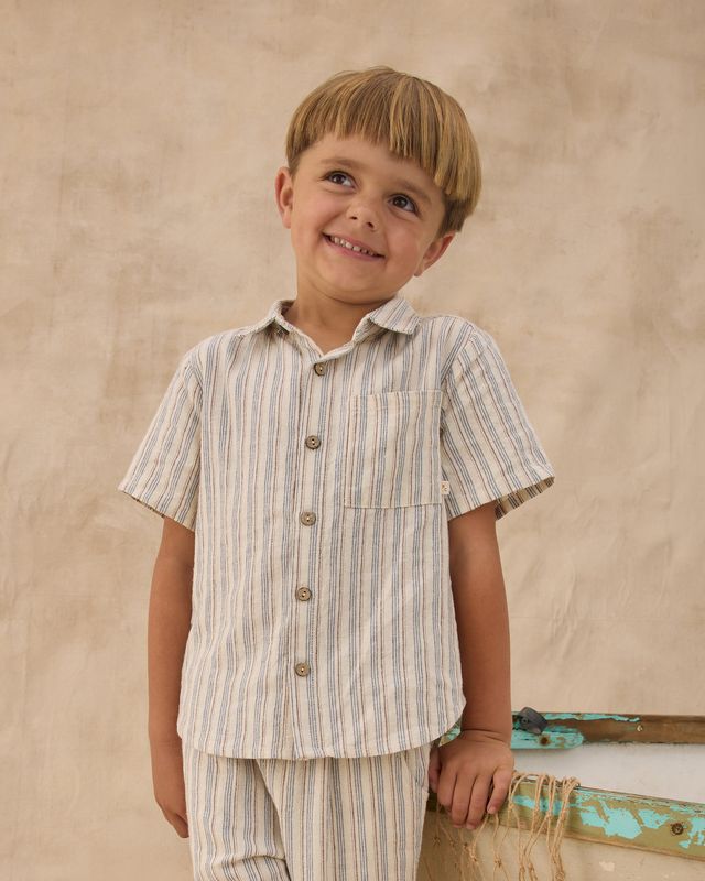 Young boy wearing a striped shirt and pants against a beige background