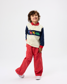 A young boy modeling a color-blocked long-sleeve polo shirt with red pants, standing against a plain white studio background.