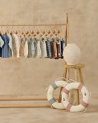 Children's clothing on a wooden rack with decorative life rings and a lamp on a stool.