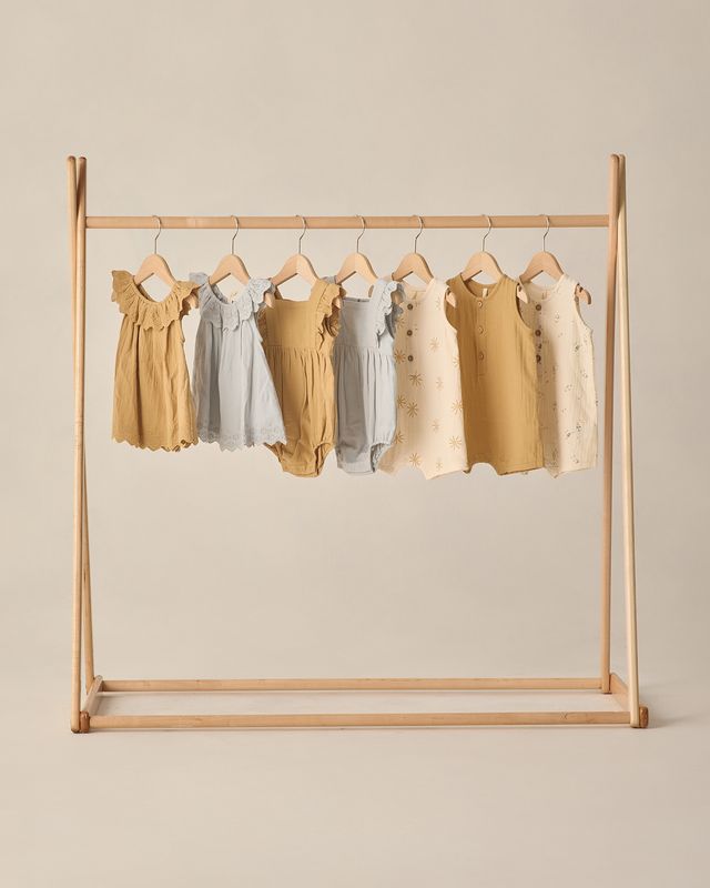 Children's dresses hanging on a wooden rack against a beige background