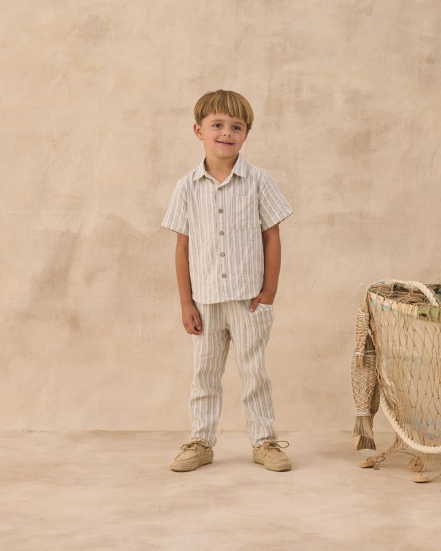 Young boy in striped shirt and pants standing next to a wicker basket against a beige background