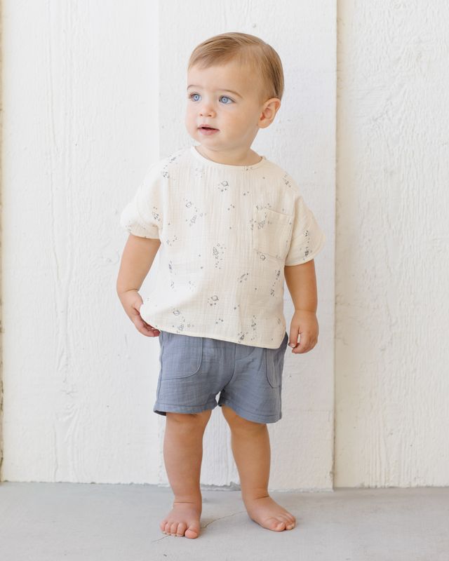 Child wearing a white shirt with small patterns and gray shorts against a white background