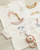 Baby outfit with t-shirt and lion rattle on a light wooden surface