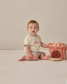 Baby sitting on a plain surface next to a decorative basket