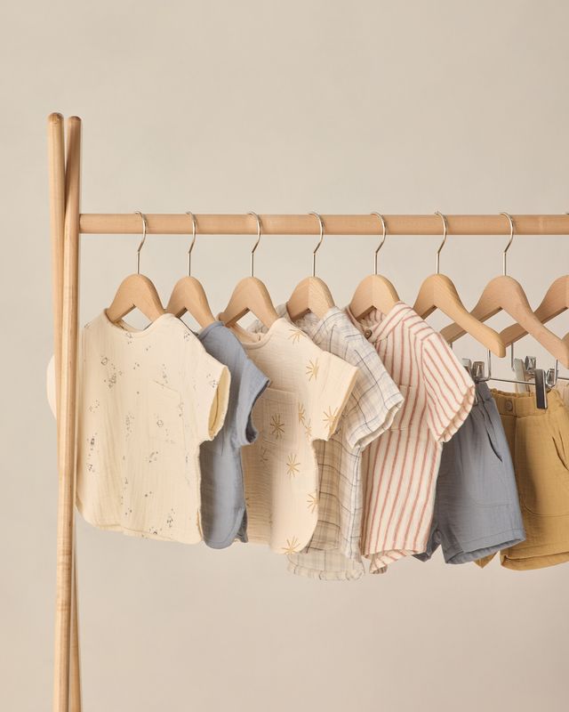 Children's clothing on wooden hangers against a beige wall