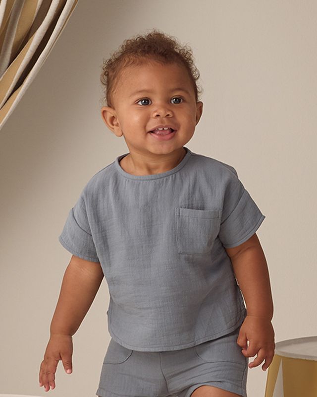 Child wearing a gray outfit standing against a neutral background