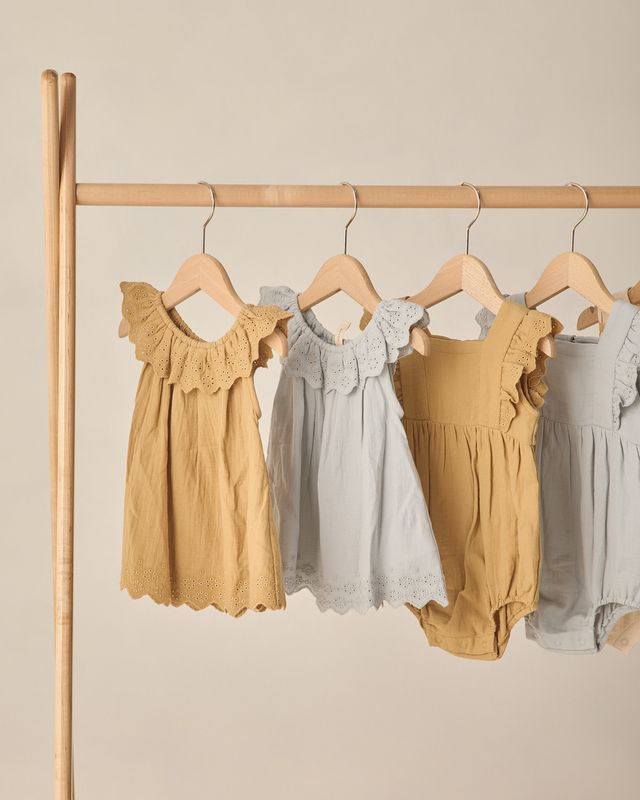 Four children's dresses in yellow and gray on hangers against a beige background